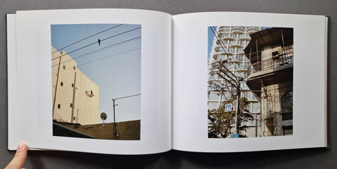 An open book, showing two printed photographs side by side. A human hand is visible at the lower left edge holding the book open.