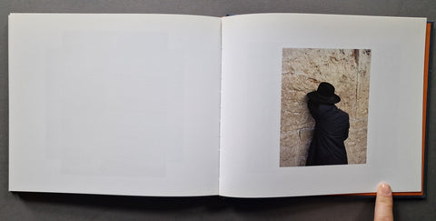 An open book, showing mostly blank white pages with a small printed photograph on the right page depicting a person in black clothing leaning against a stone wall. 