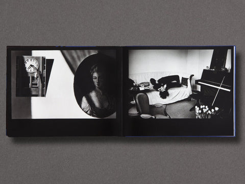An open black photo book displayed flat against a dark gray background, showing two black-and-white photographic pages with interior room scenes and a circular portrait.