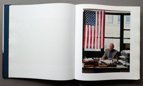 An open book, showing a large blank white page on the left and a printed photograph on the right depicting a man seated at a desk in front of an American flag.