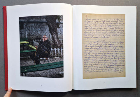 An open book laid flat on a dark surface, showing a printed photograph on the left page and a page with handwritten text on the right.