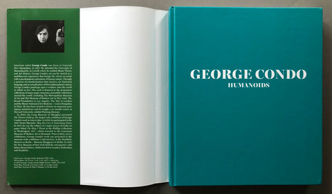 An open hardcover book titled 'GEORGE CONDO HUMANOIDS' with a teal cover, white pages, and a dark green inner spread with text and a black-and-white portrait photo, photographed from above on a dark surface.