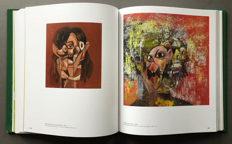 An open art book spread showing two abstract portrait paintings printed on the pages, photographed from above on a dark gray surface.
