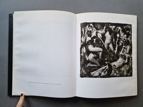 An open book showing a black-and-white reproduction of a classical sculpture on the right page, with a hand holding the left page against a dark gray background.