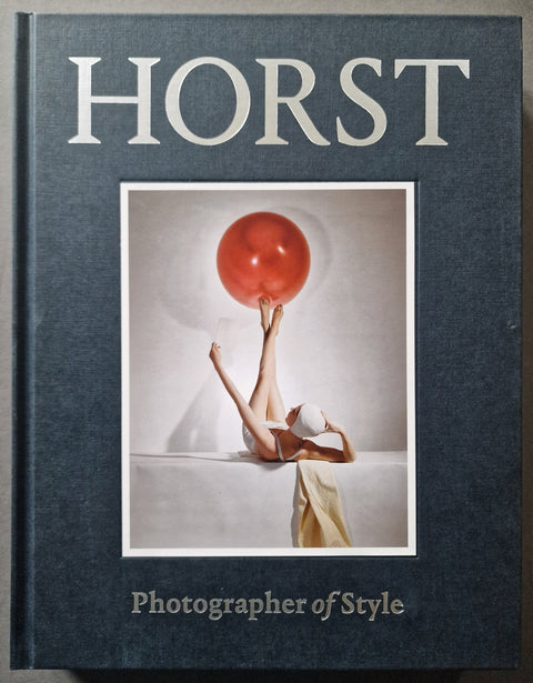 The book cover of Horst: Photographer of STyle in navy blue with a photo of a woman in white swimwear balancing a red ball with her feet in the air.