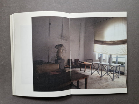 An open book spread showing a large interior photograph of a dimly lit room with tables, chairs, and a draped window treatment, photographed against a dark gray background.