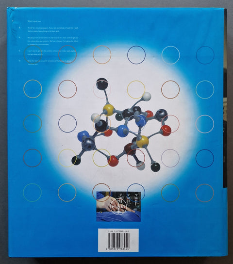 A blue book featuring a large central molecular model graphic, a grid of colored circles, small text blocks, and a barcode label near the bottom.