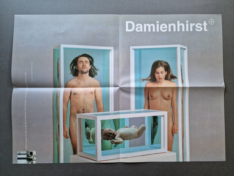 A folded Damien Hirst art poster laid flat on a dark gray surface. The print features the text 'Damienhirst' at the top and a surreal photograph of a nude man (Hirst himself) and woman (his partner at the time) standing beside glass display cases, with a baby suspended inside one case.