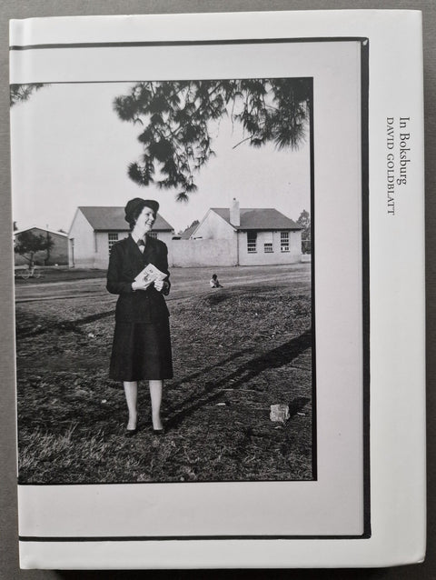 A hardcover book titled 'In Boksburg' by David Goldblatt, featuring a black and white photograph of a woman standing in a grassy field with houses in the background.