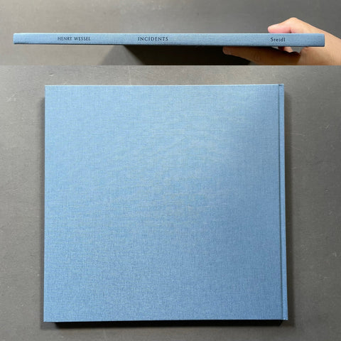 A light blue hardcover book titled 'INCIDENTS' by Henry Wessel, shown from the front cover and spine with a hand holding the spine at the top against a dark gray background.