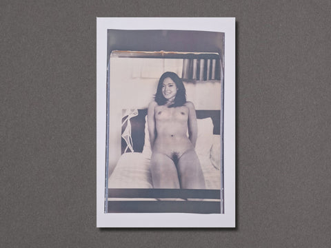 A square photographic art print with a white border, featuring a black and white vintage-style photograph of a nude woman sitting on a bed