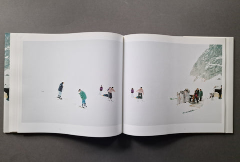 An open art book, showing two printed pages with minimalist winter scenes featuring small figures in a snowy landscape.