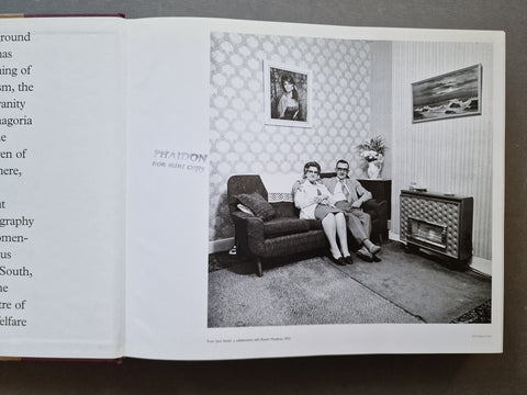 An open book spread from Martin Parr by Val Williams showing a black-and-white interior photograph of a couple sitting on a sofa in a vintage living room, with stamp on top "Phaidon non mint copy"
