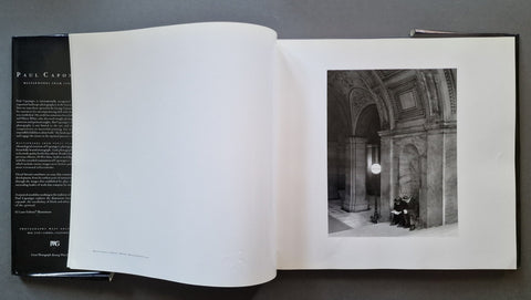 An open book showing a black-and-white architectural photograph on the right page and printed text on the left page, photographed from above on a dark gray surface.