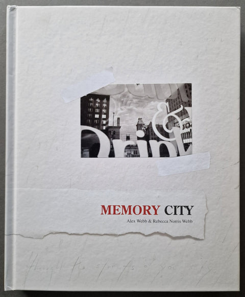 A square hardcover book titled 'MEMORY CITY' by Alex Webb and Rebecca Norris Webb, featuring a textured off-white cover with a torn-paper style graphic, a black-and-white city photograph, and red and black title text.