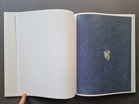  A book spread showing a large-scale negative of a person on the beach sunbathing and reading a book on the right page