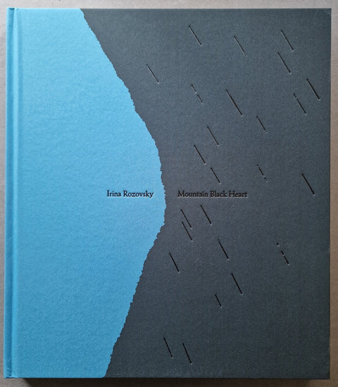 A square hardcover book titled 'Mountain Black Heart' by Irina Rozovsky, featuring a minimalist cover design with a vertical blue-to-black gradient and small cutout rain-like lines on the black side.