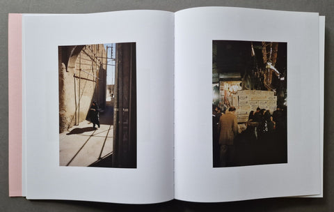 An open book, showing two printed photographs on white pages. The left page contains a warm-toned street scene with a person walking under strong sunlight, and the right page shows a darker nighttime market or street scene with several people.