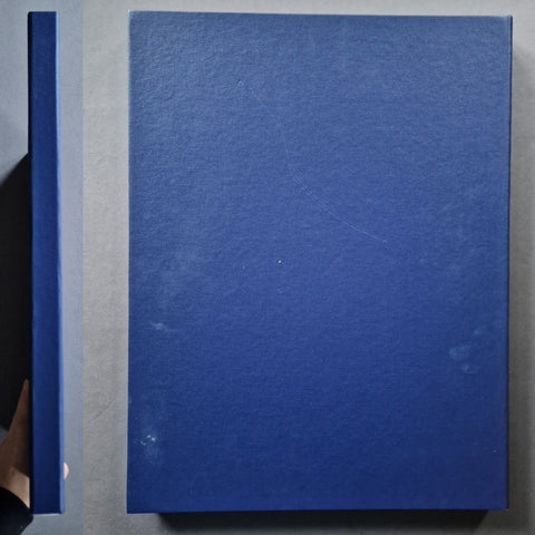 A hardcover book with a textured blue cover, shown from above with its spine visible on the left against a gray background.