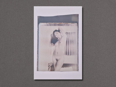 A vertical photographic art print with a white border. The photograph depicts a naked woman smiling at the camera