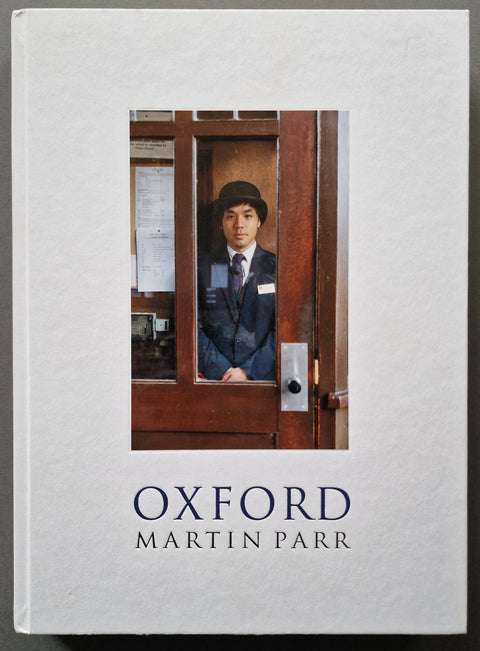 The book cover of 'Oxford' by Martin Parr, featuring a white textured background with a central photograph of a man in a uniform behind a wooden door, and the title and author name printed below.