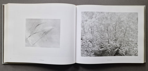 An open book showing two monochrome art prints on white pages, photographed from above on a dark gray surface.