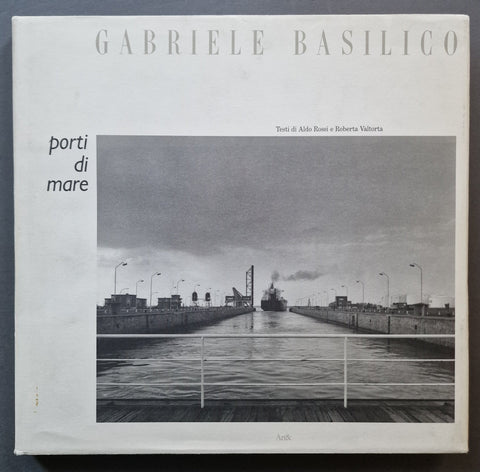 A square book titled 'GABRIELE BASILICO' and 'porti di mare' shown flat against a dark background. The cover features a black-and-white photograph of a canal or port lock with a ship in the distance, plus small text credits and the publisher mark 'Anki' near the bottom.