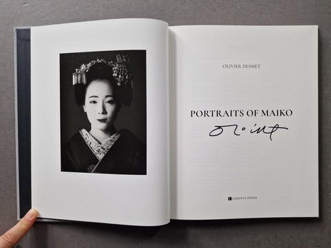 An open book titled 'Portraits of Maiko' by Olivier Desmet, featuring a black-and-white portrait of a woman in traditional Japanese attire on the left page and the title with an autograph on the right page.