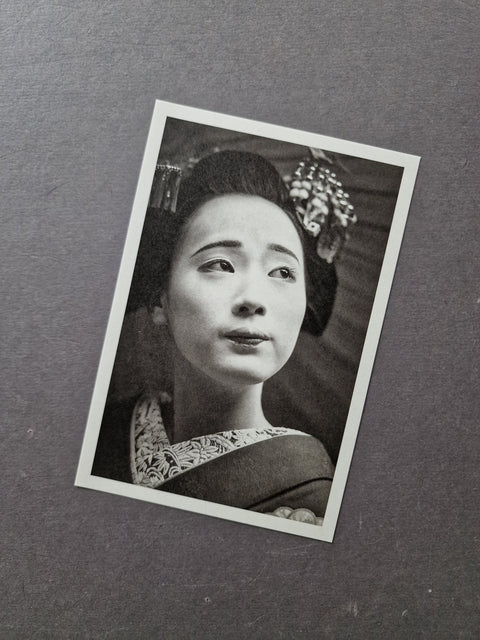 A black and white vintage-style portrait photograph print with a white border, depicting a woman in traditional Japanese attire, placed on a textured dark gray surface.