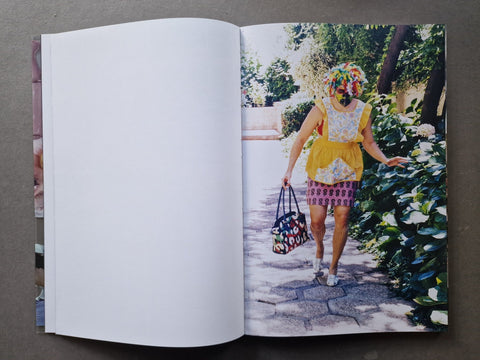 An open book, showing a large blank white left page and a printed color photograph on the right page of a woman walking outdoors in a yellow dress while carrying a patterned handbag.