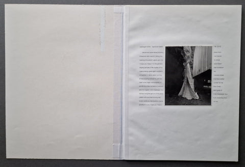 An open white art book , showing a black-and-white photograph on the right page with surrounding text, photographed against a dark gray background.