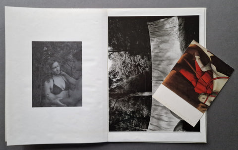 An open art book, showing a black-and-white portrait print on the left page and a black-and-white silver gelatin print on the right and a loosely laid in printed material on top.