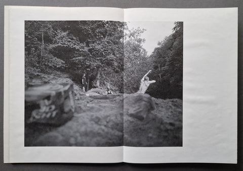 An open book showing a black-and-white photographic print of a forest trail scene with people walking among rocks and trees.