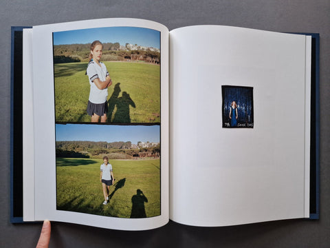 An open photo book displaying printed pages with outdoor portrait photographs and a small black-and-white portrait print on the right page, held open by a hand against a dark gray background.