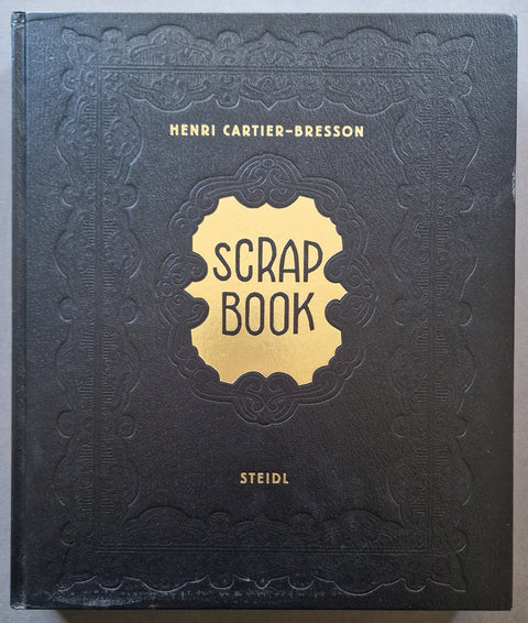 The front cover of the 'Scrap Book' book by Henri Cartier-Bresson, published by Steidl. The cover is a textured black leather-like material with an embossed decorative border, featuring a central gold shield emblem with the title 'SCRAP BOOK' in black text.