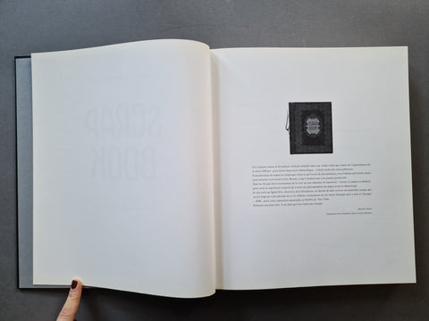 An open book, showing a mostly white interior spread with faint large text on the left page and a small black square image with text on the right page. 