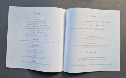 An open printed booklet or program spread photographed from above on a dark gray surface. The pages contain small black text, including a table of contents and program text, with no people or real environment beyond the tabletop background.
