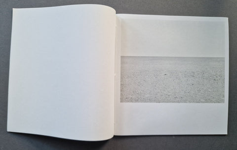 An open book showing a minimalist landscape photograph of a flat, textured gray plain on a white page, set against a dark gray background.