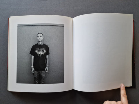 An open book, showing a black-and-white printed portrait of a man wearing a black graphic T-shirt on the left page, with an empty white page on the right. 