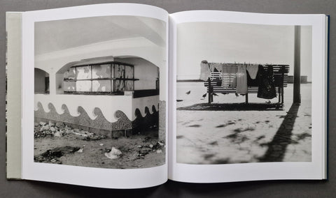 An open book showing two black-and-white photographic prints side by side on white pages, photographed from above on a dark surface.