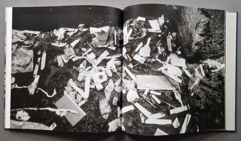 An open book showing a black-and-white photographic print of scattered debris or trash on the ground, photographed from above on a dark surface.