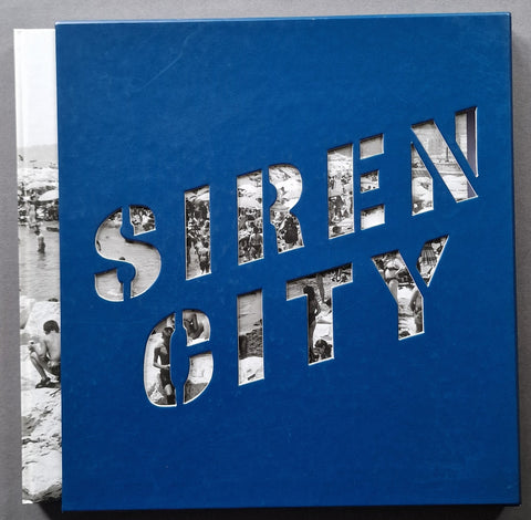 A square blue book cover titled 'SIREN CITY' with cutout lettering revealing black-and-white photographs, photographed against a neutral gray background.
