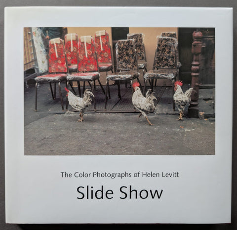 The book cover of 'The Color Photographs of Helen Levitt Slide Show' showing a white cover with a central color photograph of chickens walking past rows of patterned chairs, with the title printed below.