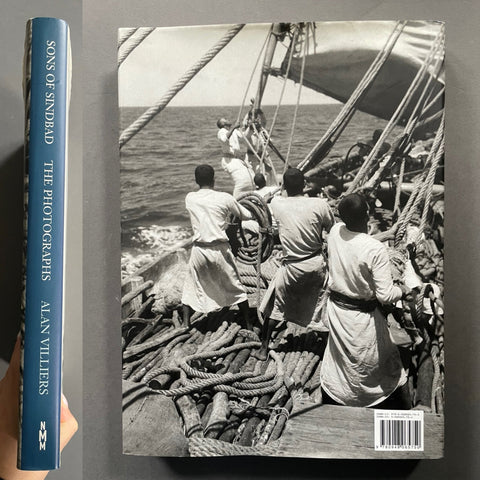 A hardcover book titled "Sons of Sindbad: The Photographs" by Alan Villiers, shown standing upright with its blue spine visible on the left and the front cover featuring a black-and-white photograph of people on a ship deck on the right.