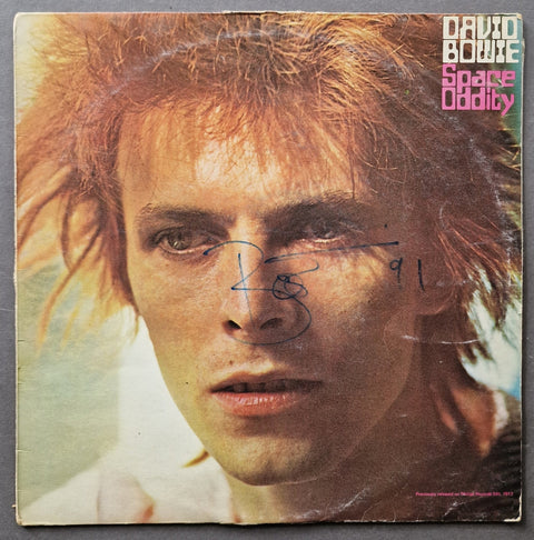 David Bowie 'Space Oddity' vinyl record cover, signed with a blue ink signature across the center, photographed flat against a dark gray background.
