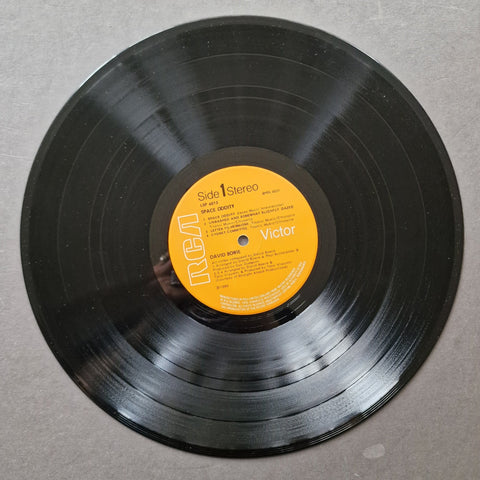 A black vinyl record with a yellow-orange RCA Victor label, photographed from above on a gray textured surface.