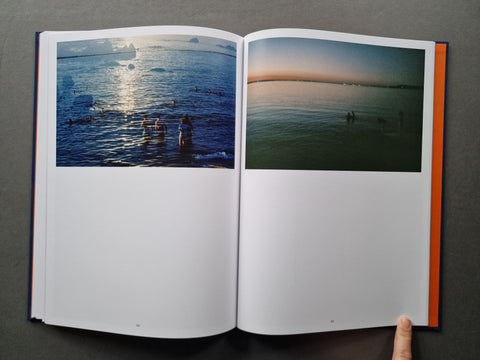 An open hardcover book laid flat on a dark gray surface, showing two printed pages with landscape photographs of icy water and figures in the scene. 