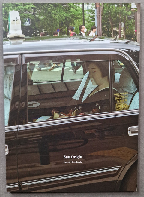 A square book cover featuring a photograph of a woman seated inside a black taxi in an urban street scene, with the title 'Sun Origin' and 'Jason Hendry' printed near the bottom.