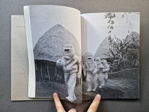 An open book spread showing a full bleed black and white photo of men in costumes in a village