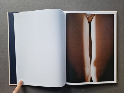 An open art book  showing a blank white page on the left and a photographic print of a close-up body image on the right. 